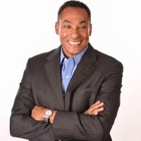 African American man, facing forward, waste up, blue shirt, dark-colored jacket