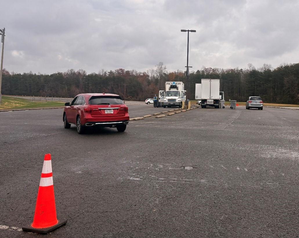 Red car driving up to shred truck in PWC Stadium parking lot area