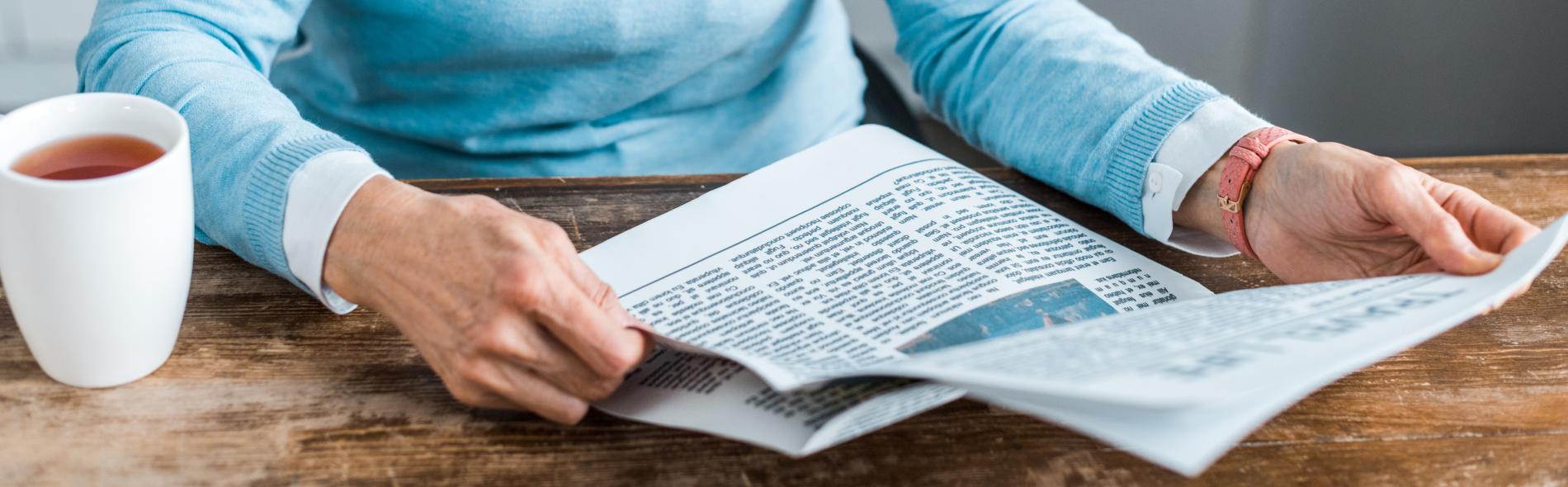 Woman holding newspaper with cup of coffee