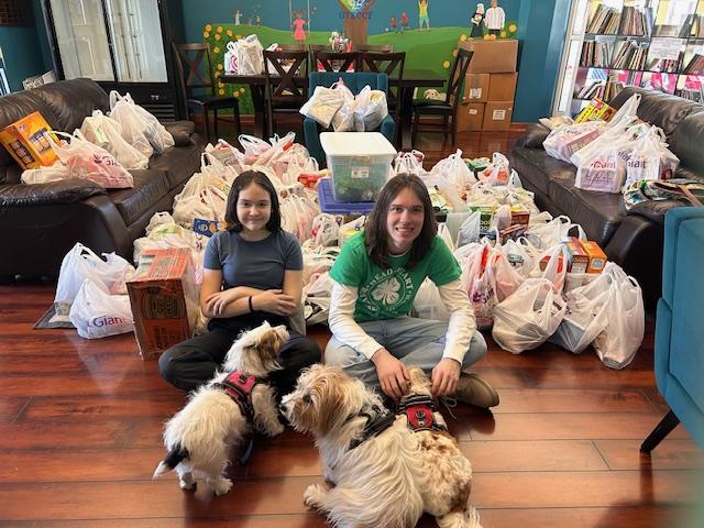 Prince William 4-H'ers with their dogs in front of a pile of bags of food donations for a food drive.